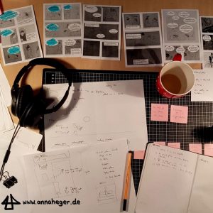 Foto: viele Blätter mit ausgedruckten Comicentwürfen und Korrekturen liegen auf einem Schreibtisch, ausserdem pinke Post-it Notzizettel, ein Notizbuch und eine Teetasse.