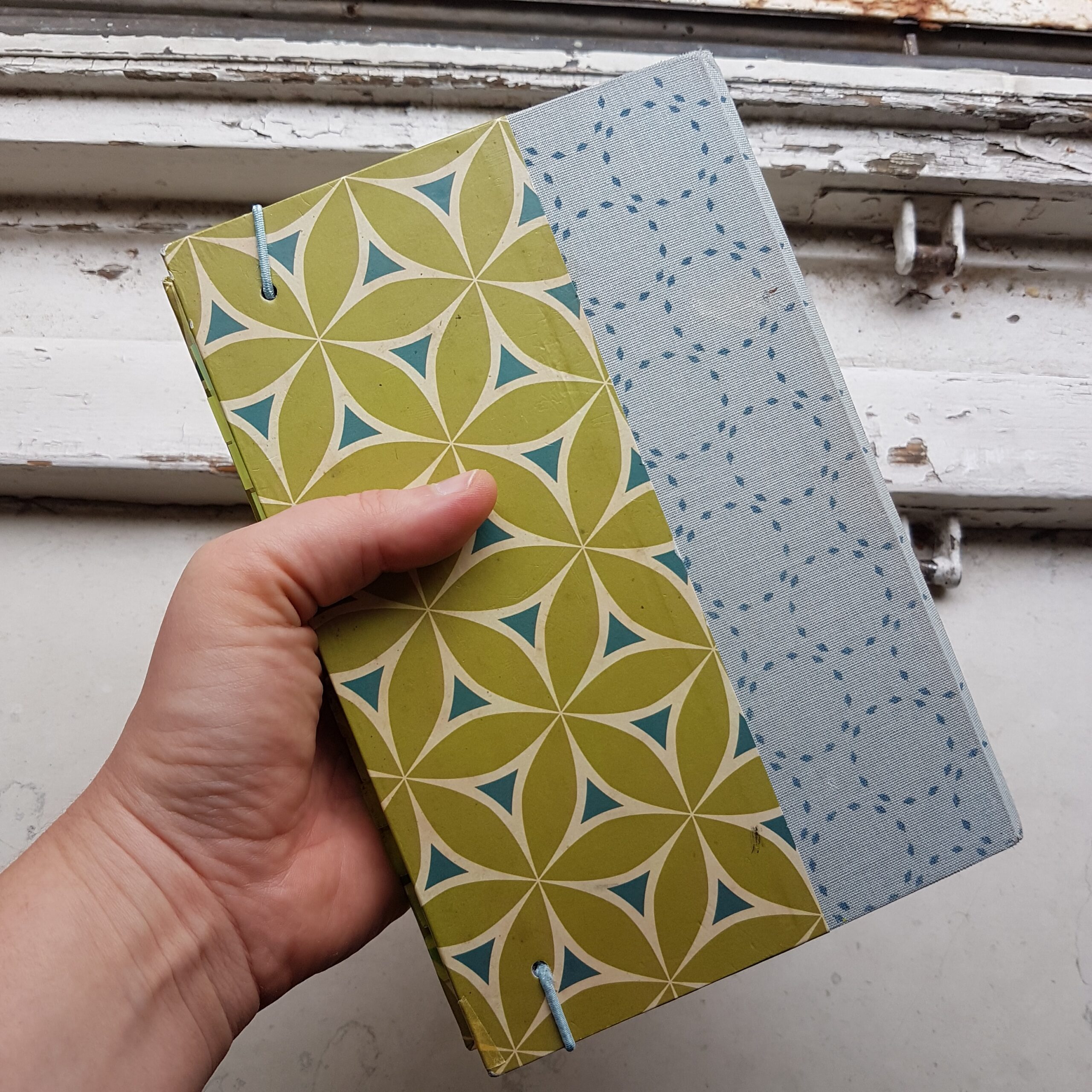 Cover vom Skizzenbuch mit grünem grafischen Muster aus Blütenblättern und breitem blauem Geweberücken in blau mit gepunkteten Kreisen.