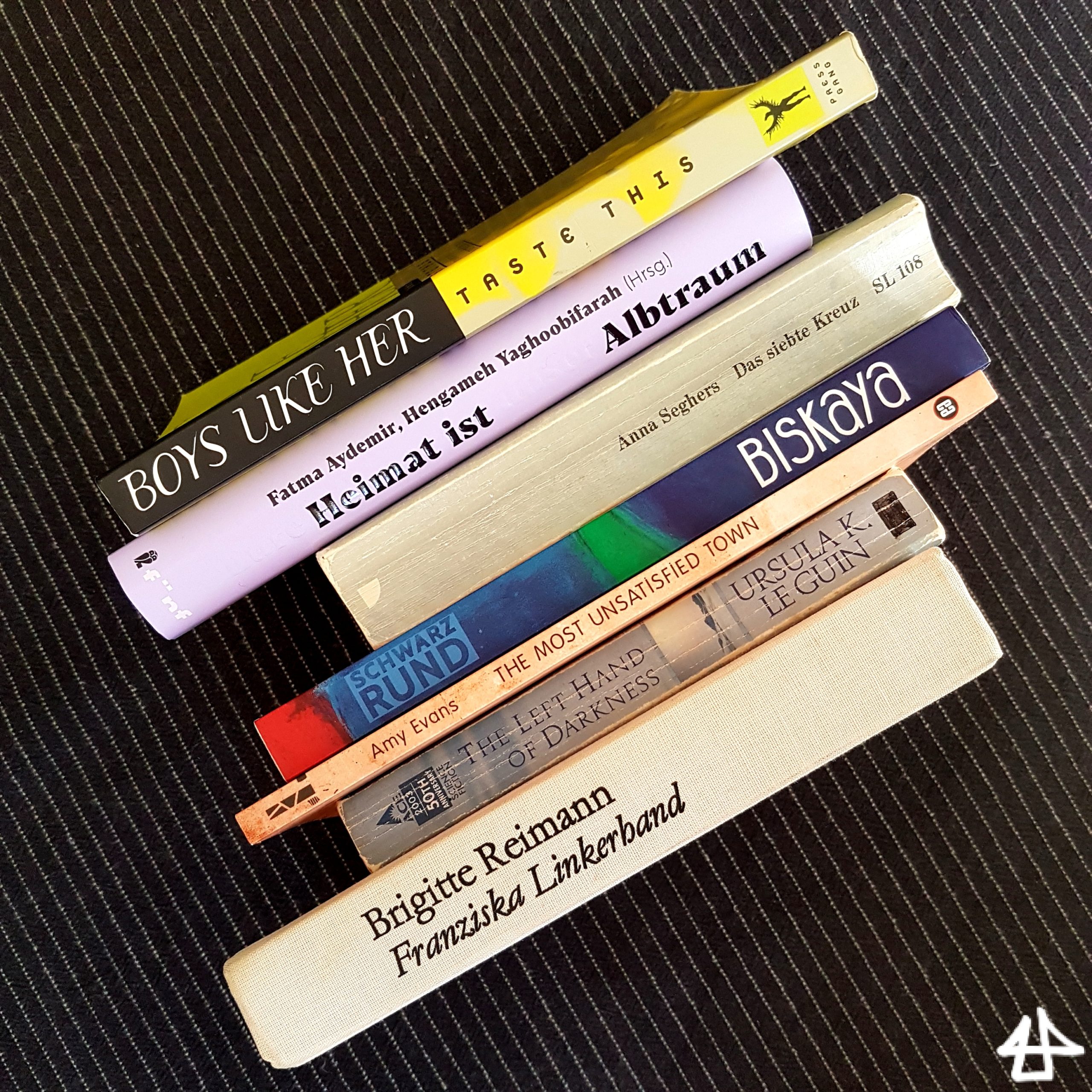 7 Bücher auf schwarzer Tischdecke. Die Titel sind: »Boys like her«, »Eure Heimat ist unser Albtraum«, »Das siebte Kreuz«, »Biskaya«, »The most unsatisfied town«, »The left hand of darkness«, »Franziska Linkerhand«