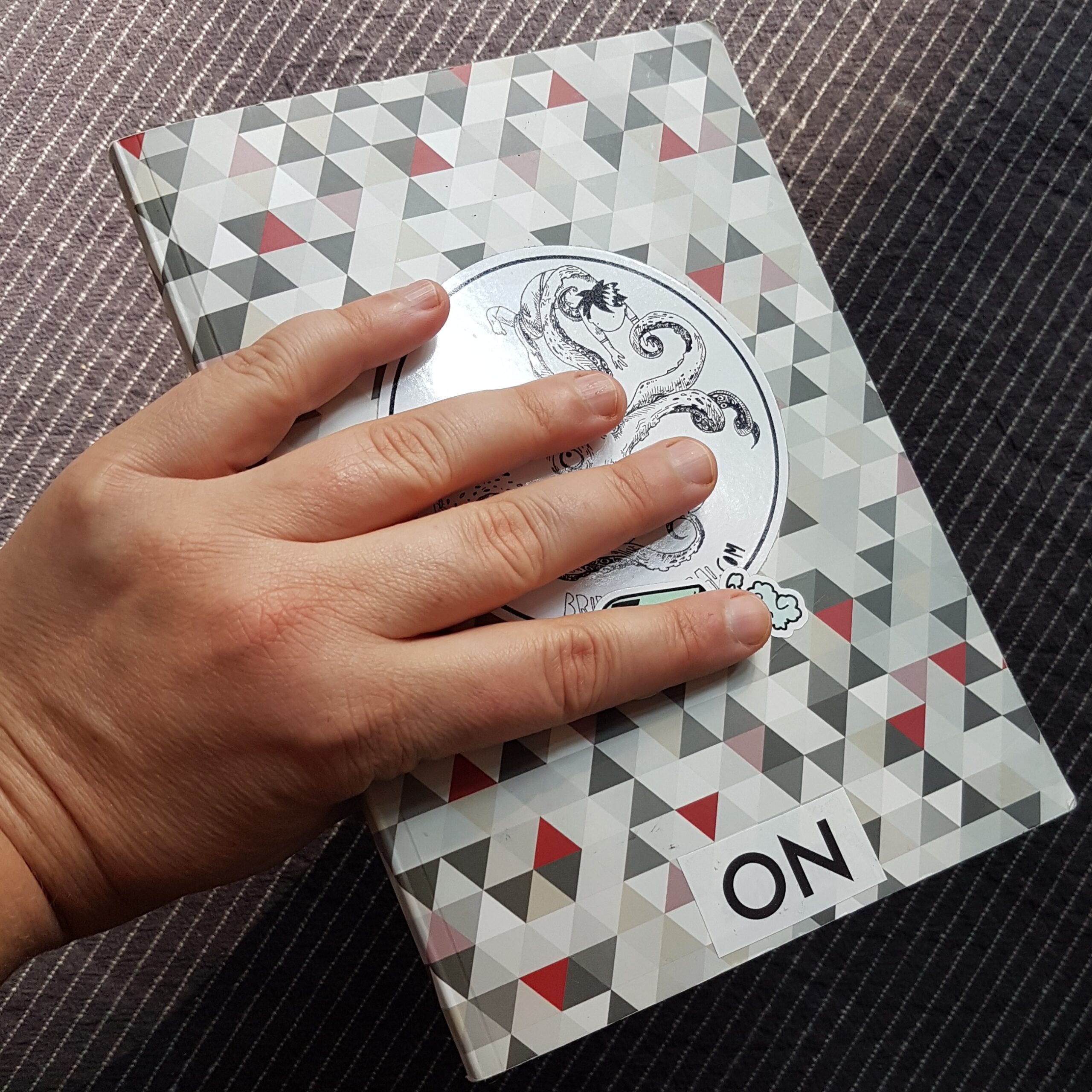 Foto vom A5 Skizzenbuch mit symmetrischen Muster aus bunten Dreiecken und rundem Aufkleber in meiner Hand