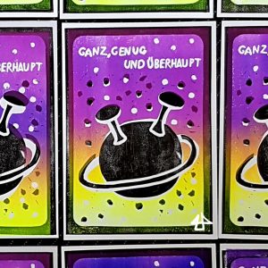 Linoldruck-Postkarte Farbverteilung des Farbübergangs von oben lila nach unten gelb und schwarz. In schwarz ein Planet mit einer Umlaufbahn und zwei großen Antennen und oben ausgespart weiß der Text in Großbuchstaben: Ganz, genug und überhaupt.