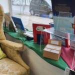 Image of the small minicomics box on a low windowsill next to a wingback chair at Buch-Kempter in Ottobrunn