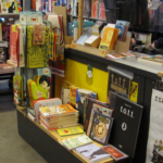 Minicomics box on the counter at Modern Graphics comic store full of small and large tables full of comics.