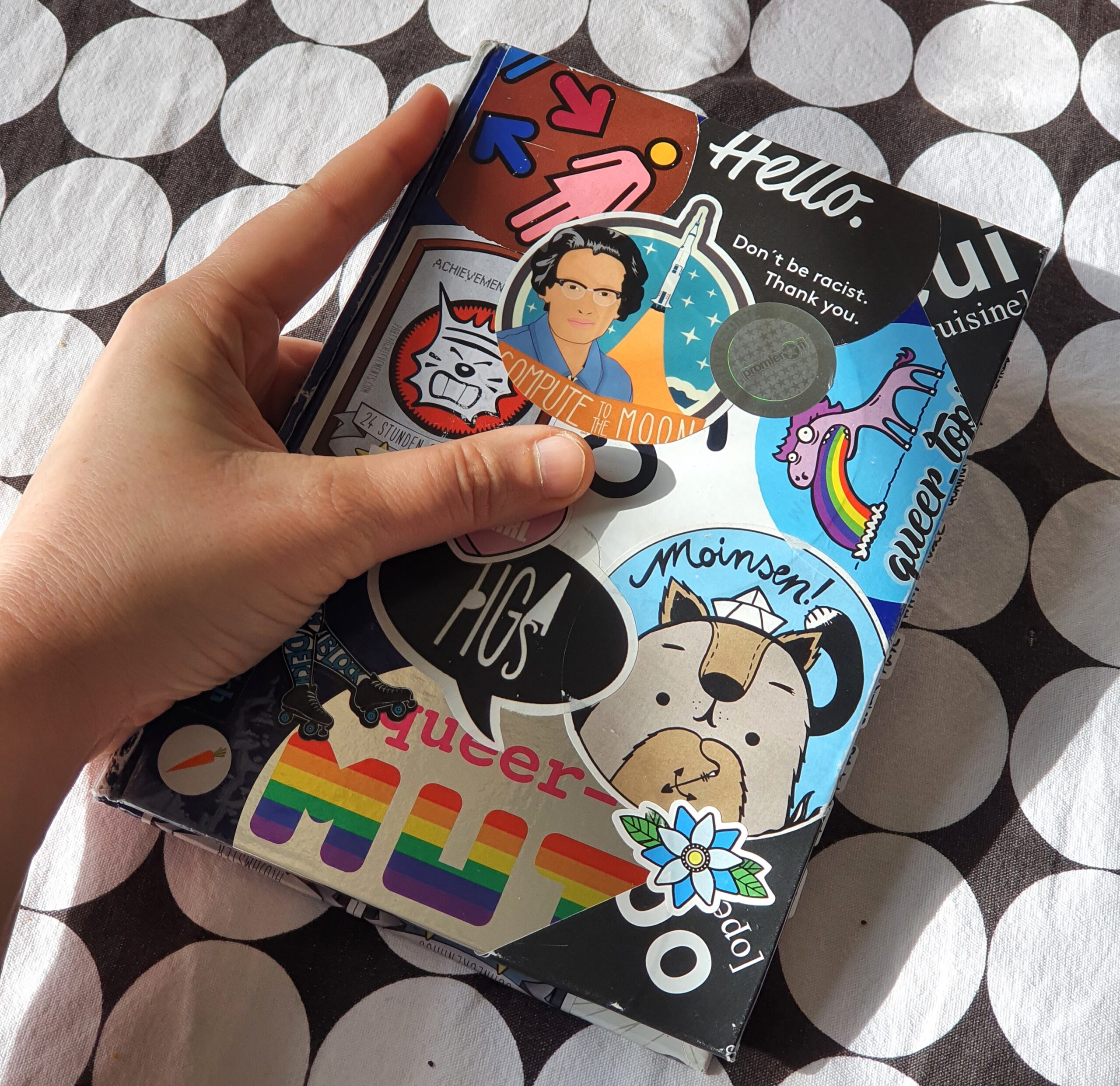 Cover vom Skizzenbuch mit übereinandergeklebten bunten Aufklebern, auch mit Text: queer, Mut, Moinsen, Hugs, Hello.