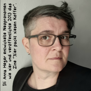 Porträtfoto von Illi mit Sidecut, wuscheligen Haaren, roßer dunkler Brill und schwarzem Jacket.  Text am linken Rand von unten nach oben: Illi Anna Heger entwickelte Neopronomen  wie xier und veröffentlichte 2013 das  Zine -Xier packt xiesen Koffer-.