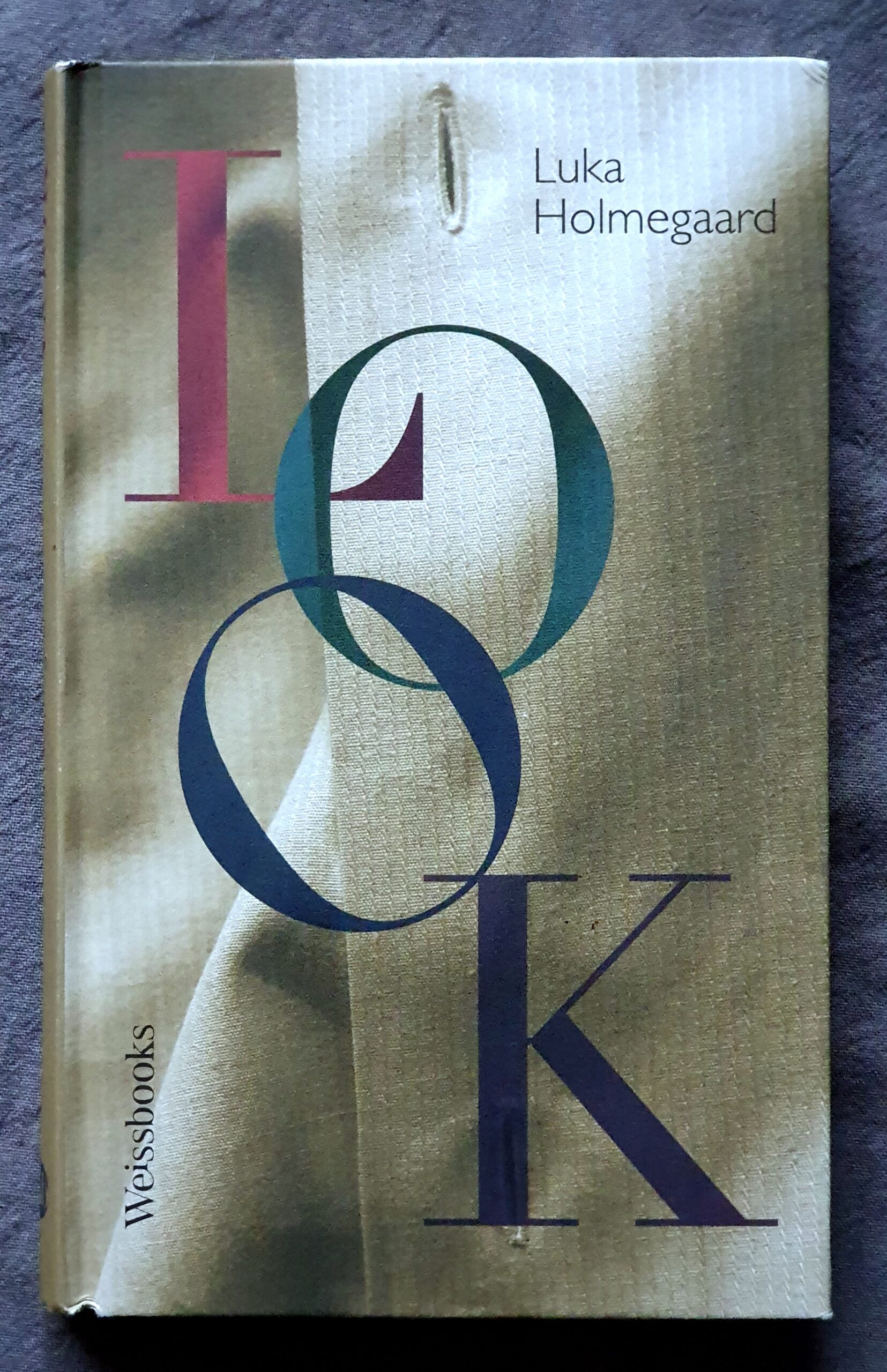 Foto des Buchcovers von 'Look', von Luka Holmegaard, bei Weissbooks. Die vier Buchstaben des Titel sehr groß in pink, grün und zwei Blautönen übereinander, im Hintergrund der Stoff eines Hemdes mit Knopflöchern. Der Name oben rechts, und der Verlag unten links.