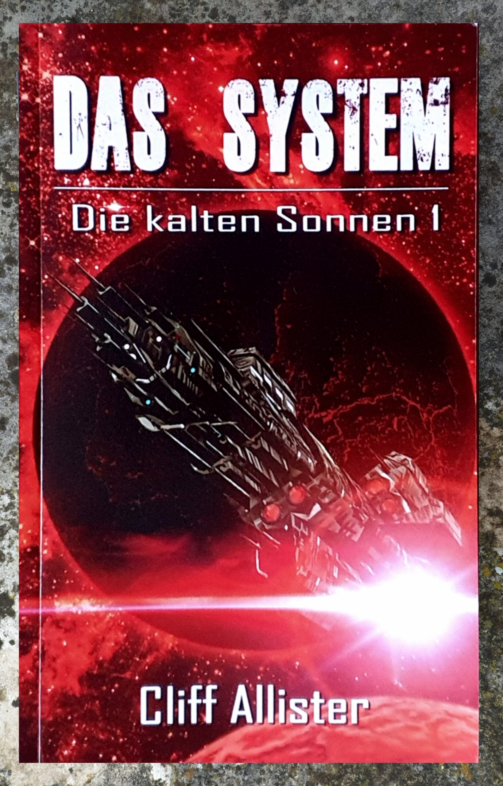 Buchdeckel von: Das System - Die Kalten Sonnen 1. Dieser Titel und der Autor, Cliff Allister, erscheinen weiß gedruckt vor dem rötlich eingefärbten realistisch gezeichneten Bildes eines schwarzen länglichen Raumschiffes, das über einem Planeten fliegt, dahinter das gleißende Licht einer Sonne.