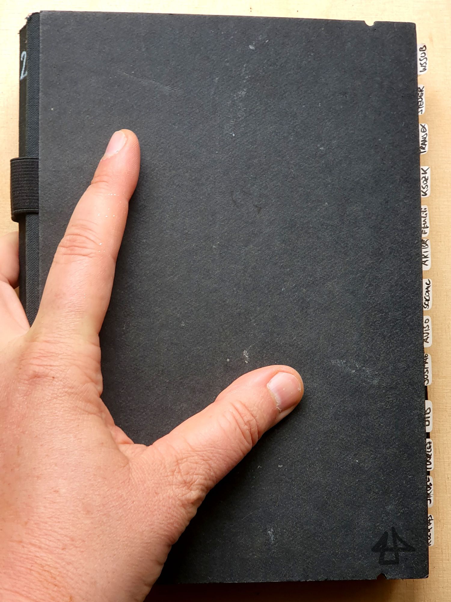 Foto einer Hand auf einem schwarzen Skizzenbuch mit kleinen Haftnotizen die am rechten Rand hervorkucken.