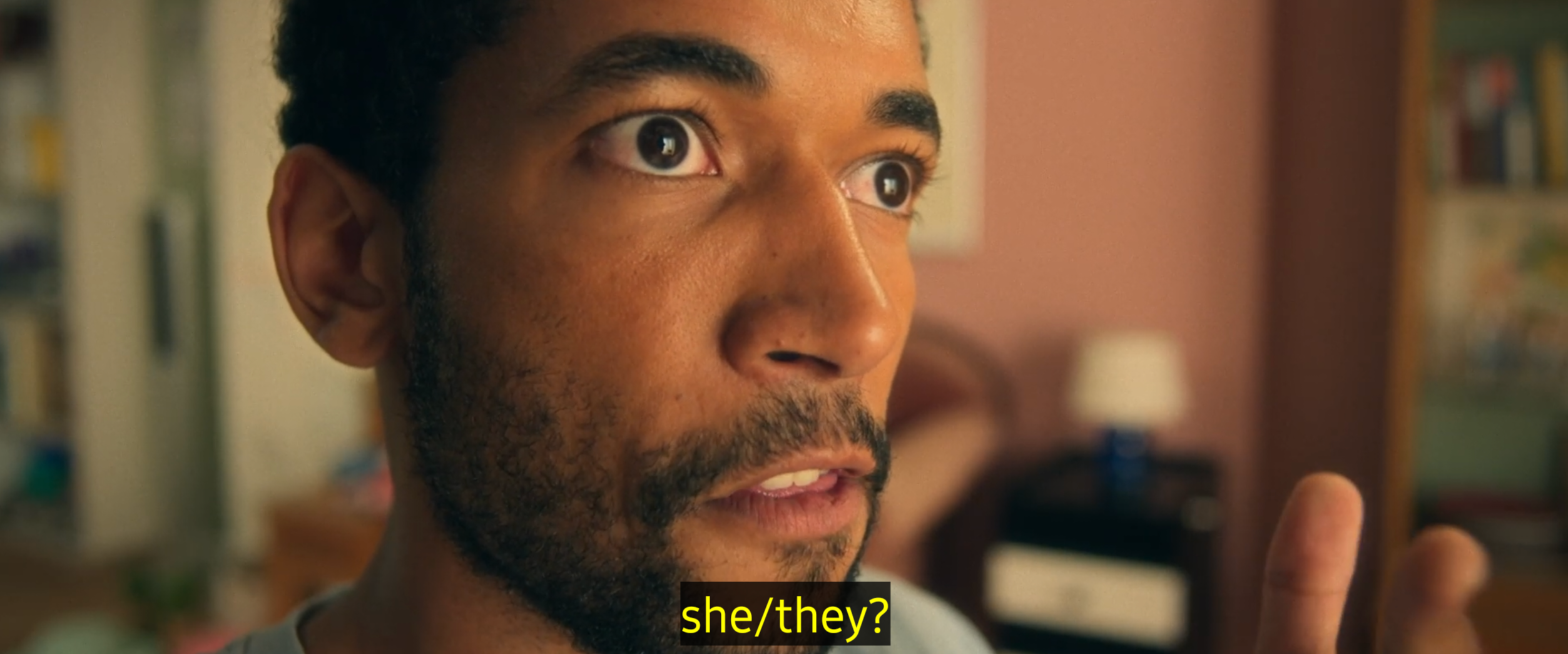 Großaufnahme des Gesichtes einer Person mit kurzem Bart, kurzen Haaren und aufgerissenen Augen. Untertitel: she/they?