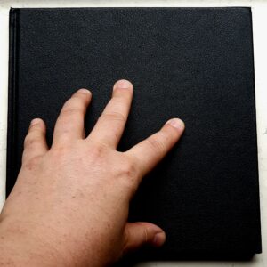 Foto einer Hand die auf einem quadratischen schwarzen Skiizenbuch ruht.